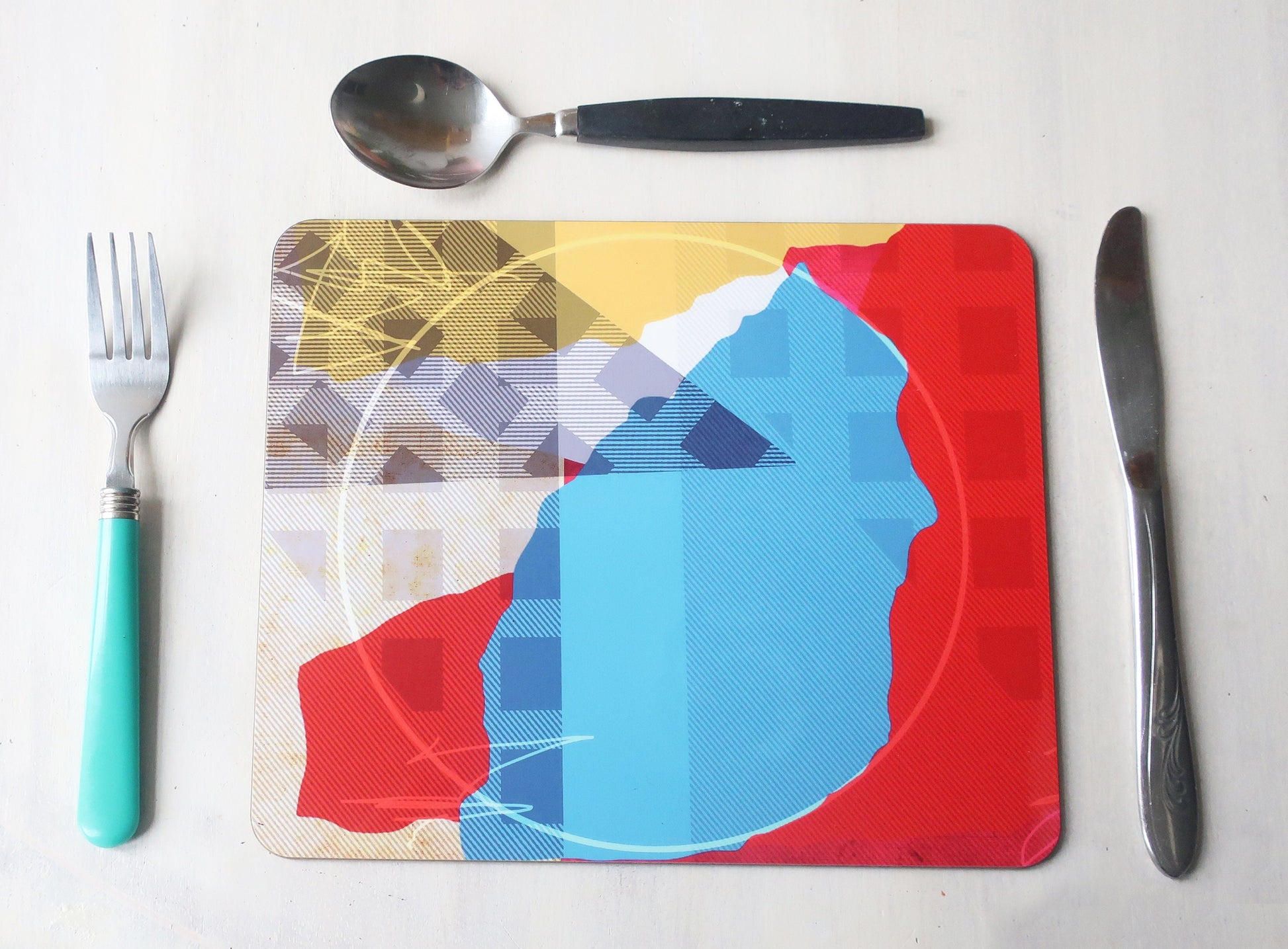 Colorful placemat with abstract design on a white surface with cutlery.