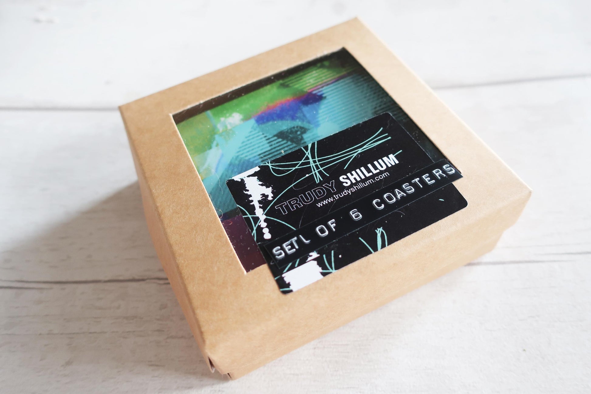 Kraft paper box with a window displaying coasters and 'Trudy Shillum' branding on a light wooden surface.