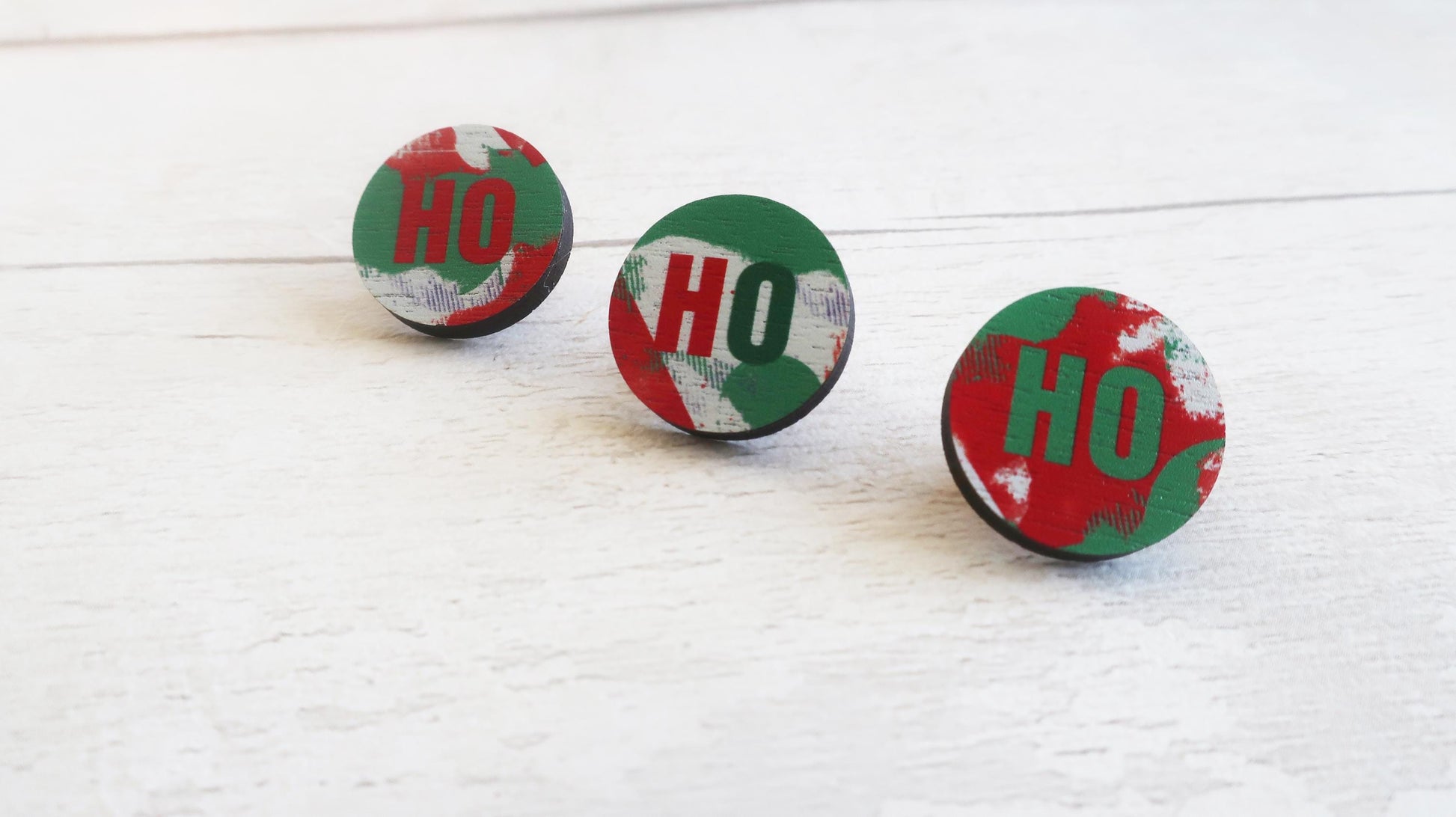 Three round pin badges with 'HO' text on a white wooden surface