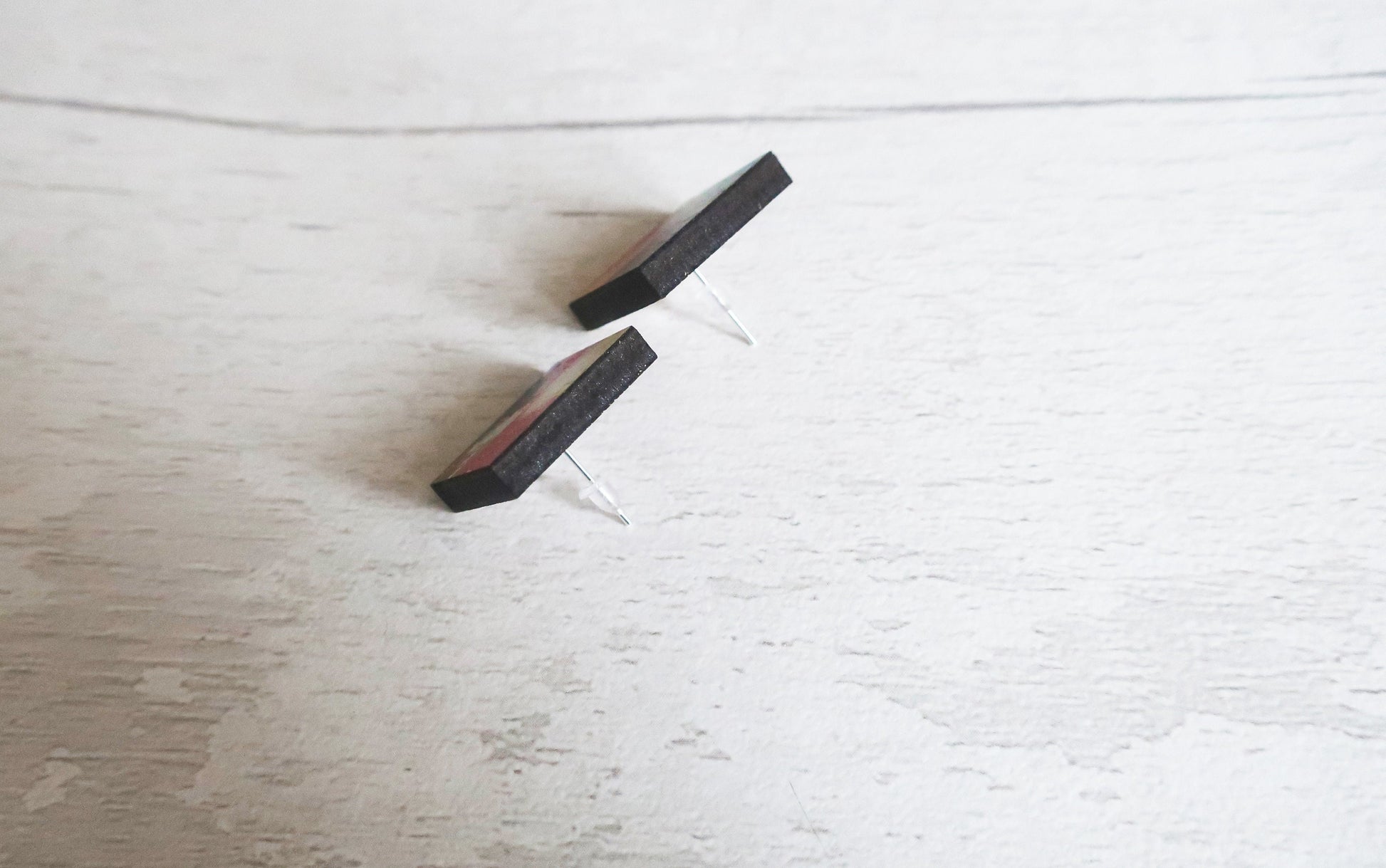 Two earrings from the side on a light wooden surface