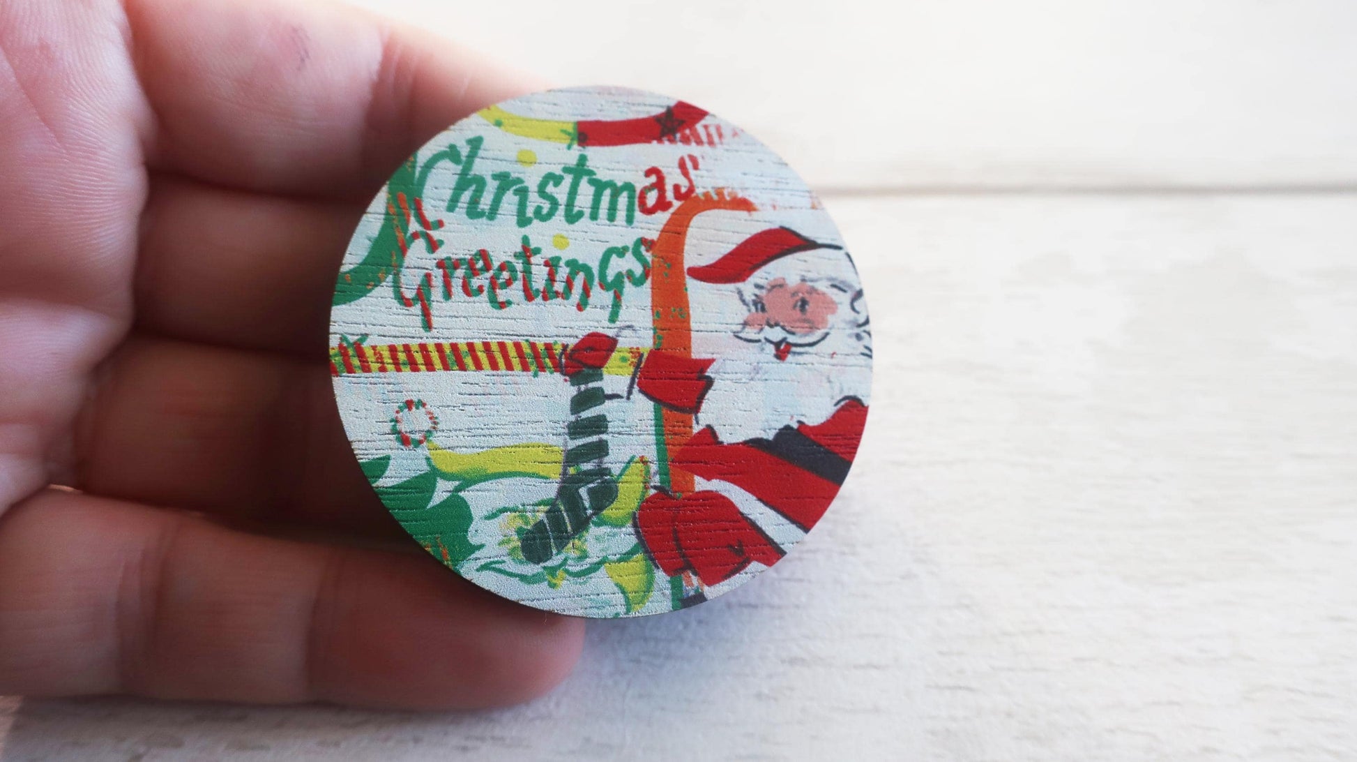 Round Christmas-themed badge  held by a hand on a light background