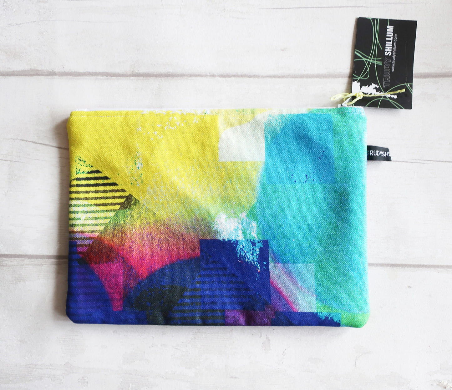 Colorful abstract pouch on a white wooden surface with a brand tag.