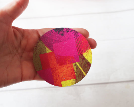 Colorful circular brooch held by a hand on a white background