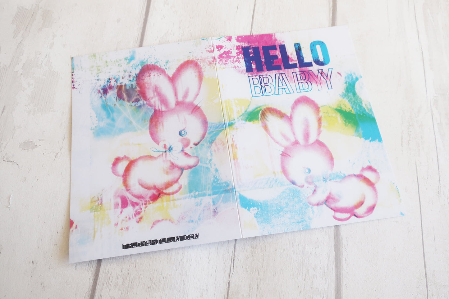 Colorful greeting card with a rabbit illustration and 'Hello Baby!' text on a wooden surface.