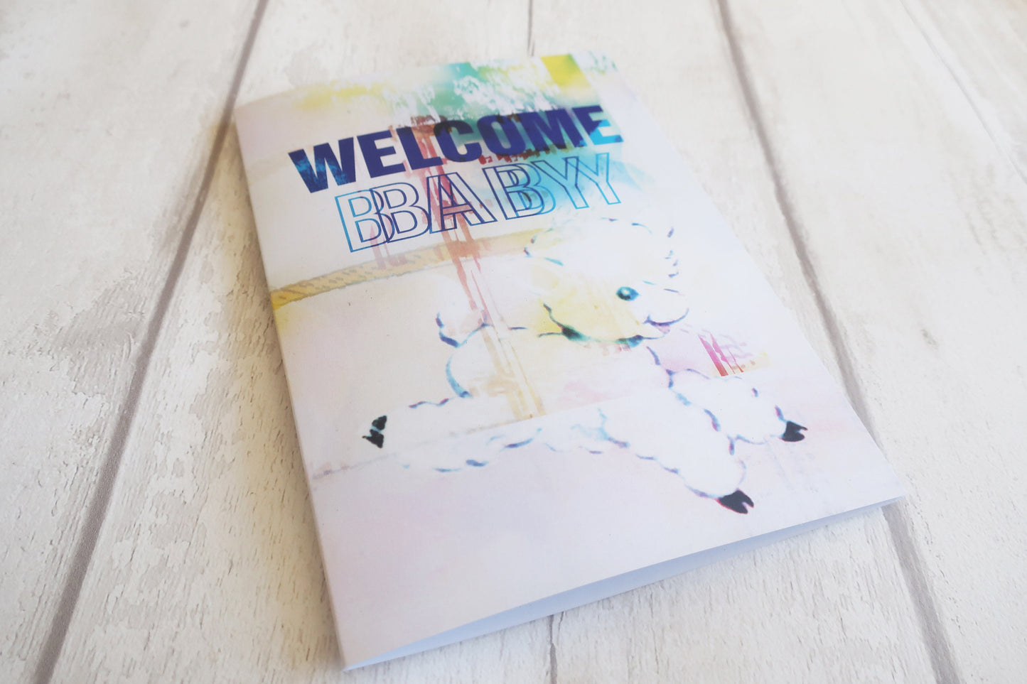 Greeting card with 'Welcome Baby' text on a light wooden surface