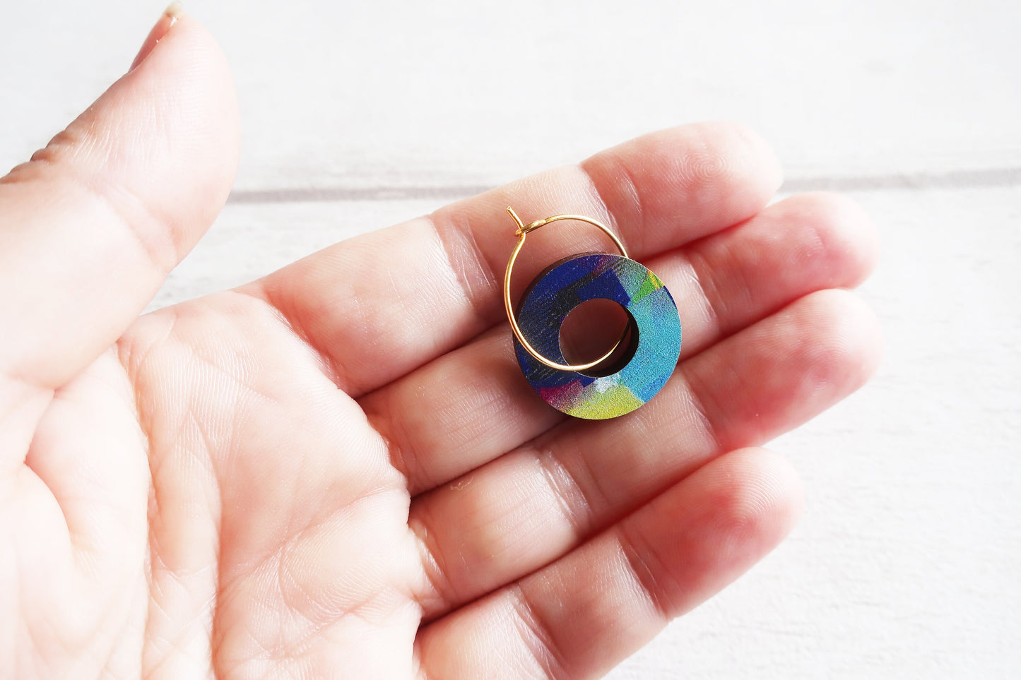 Colorful circular earring held in a hand against a white background