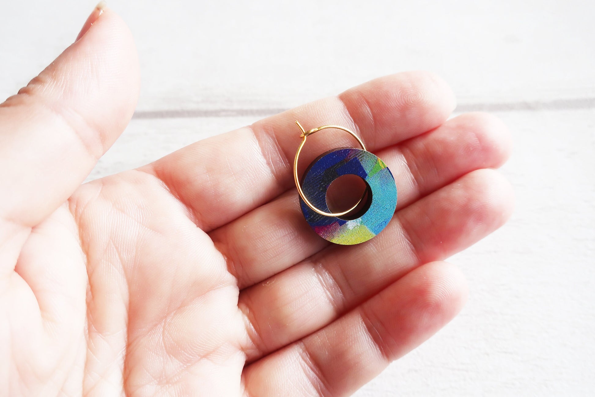 Colorful circular earring held in a hand against a white background