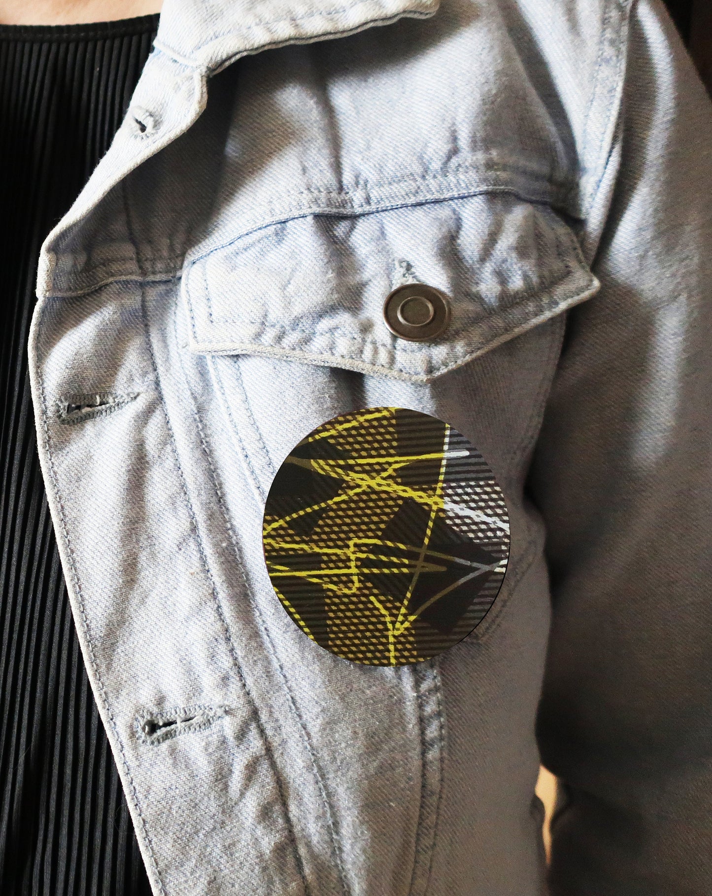 Light blue denim jacket with a circular brooch featuring yellow and black design.