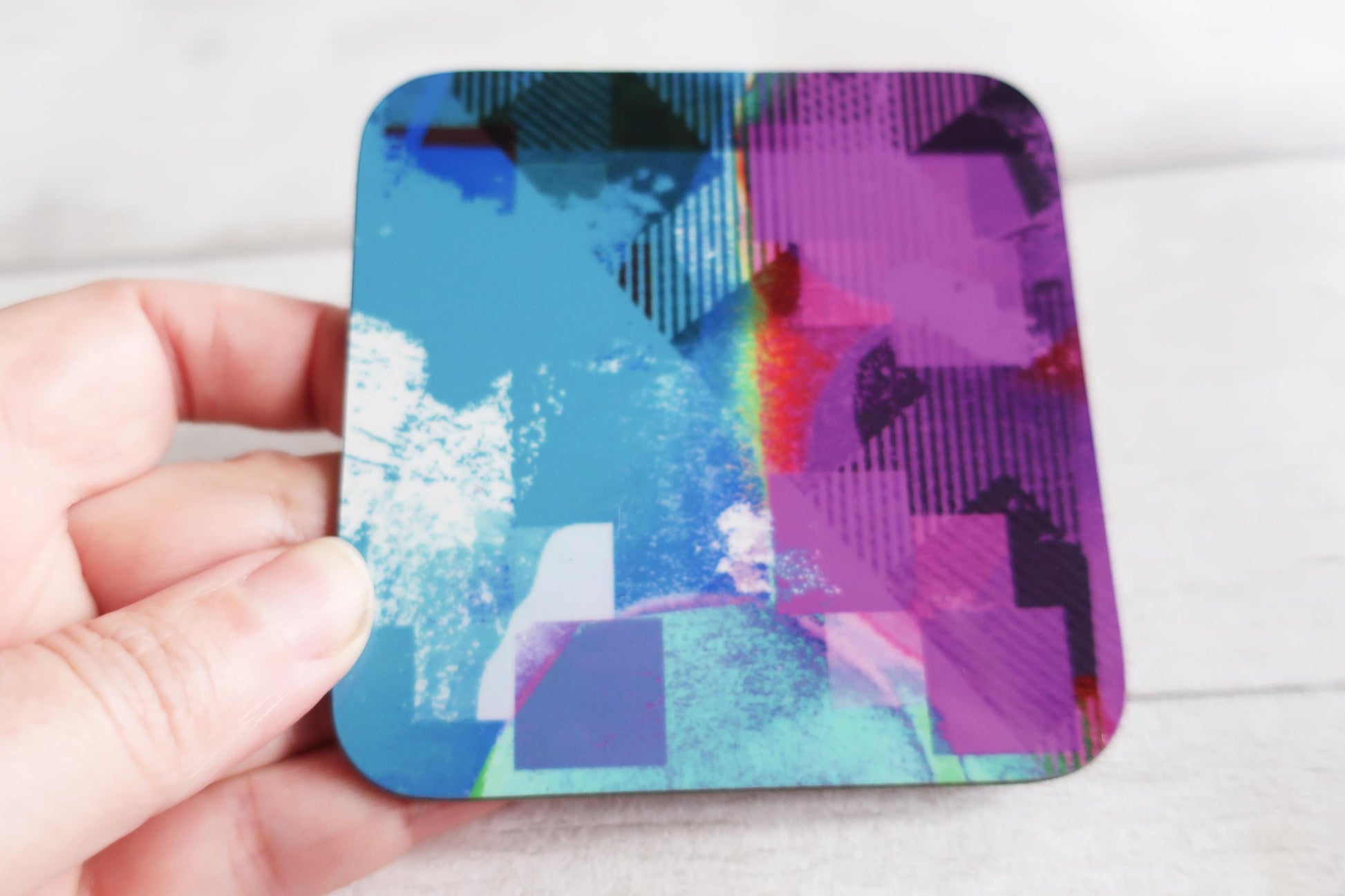 Colorful abstract design coaster held by a hand against a white background