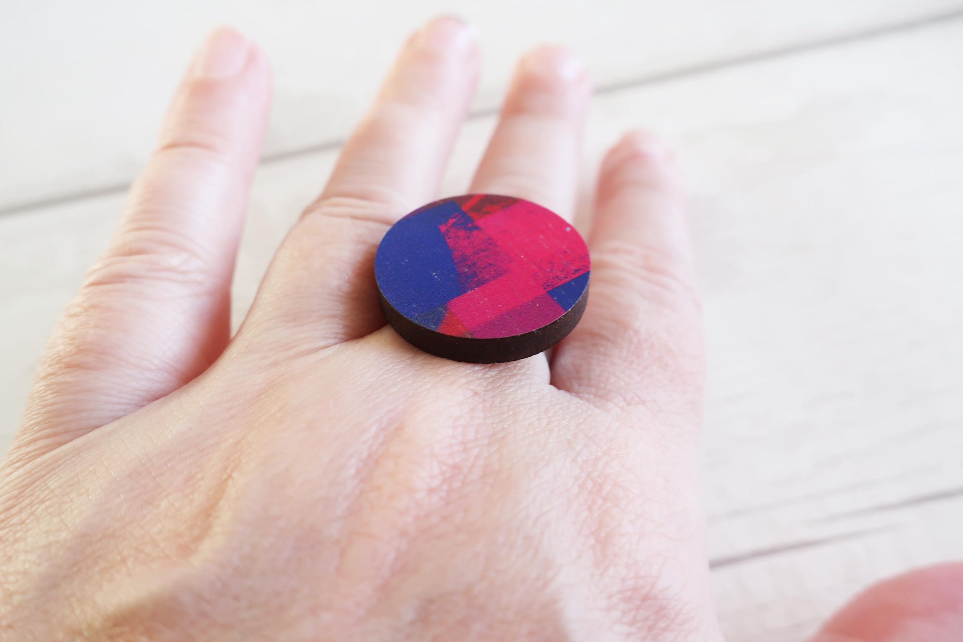Hand wearing a colorful ring on a light wooden surface