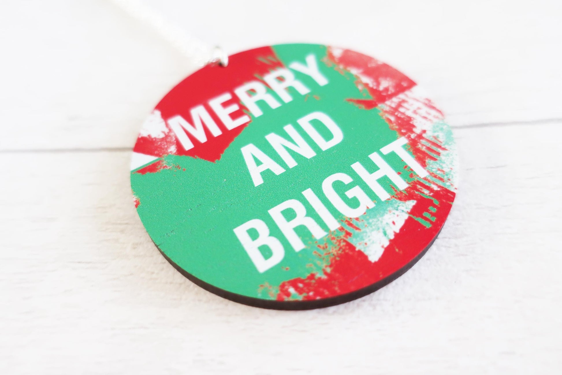 Round green and red necklace  with 'Merry and Bright' text on a white wooden surface