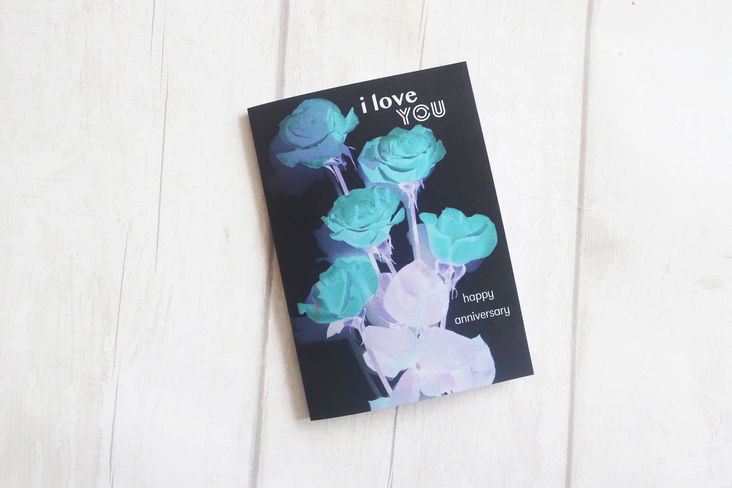 Greeting card with blue roses and 'I love you' text on a white wooden surface