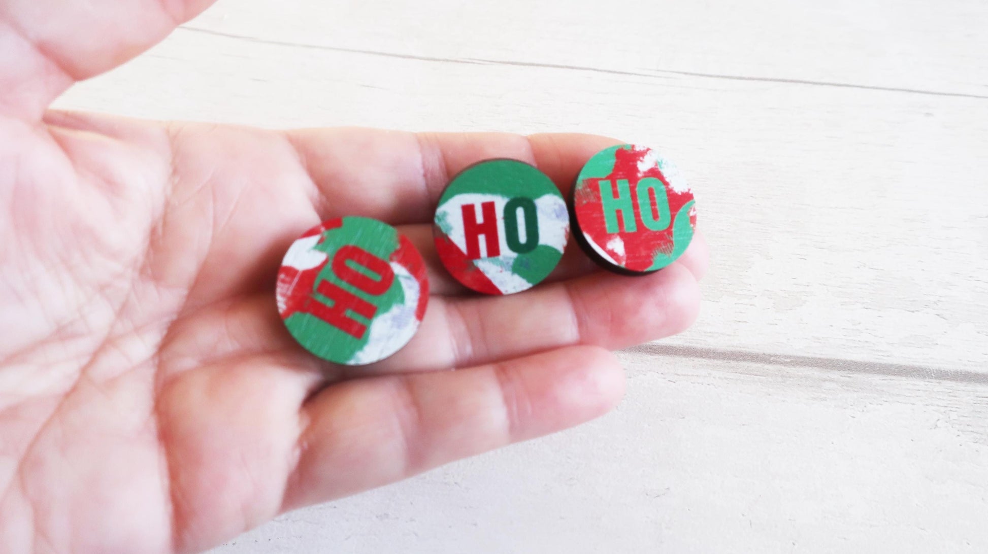 Three decorative pin badges with 'HO' text held in a hand on a light background