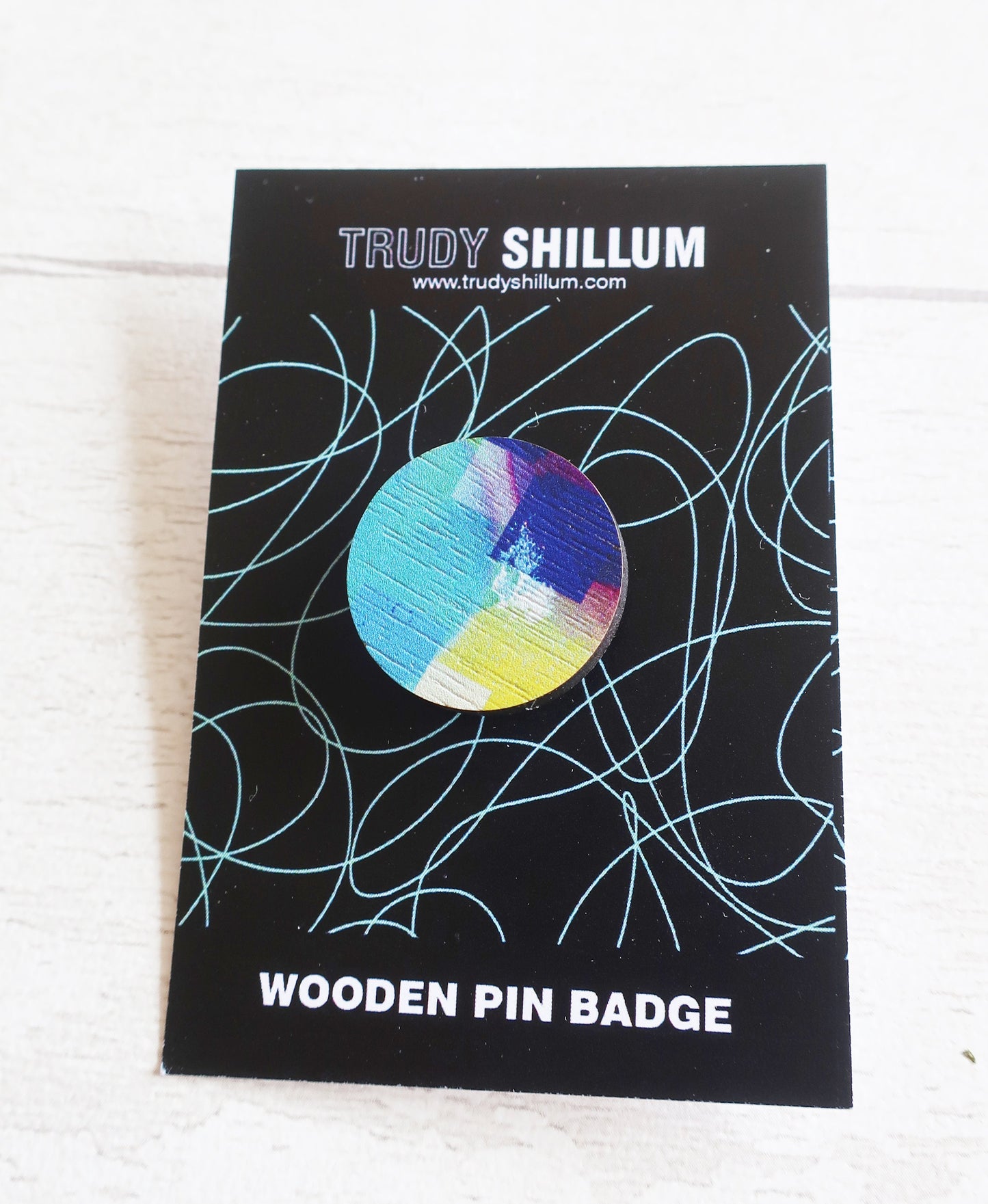 Wooden pin badge by Trudy Shillum on a black card with decorative lines