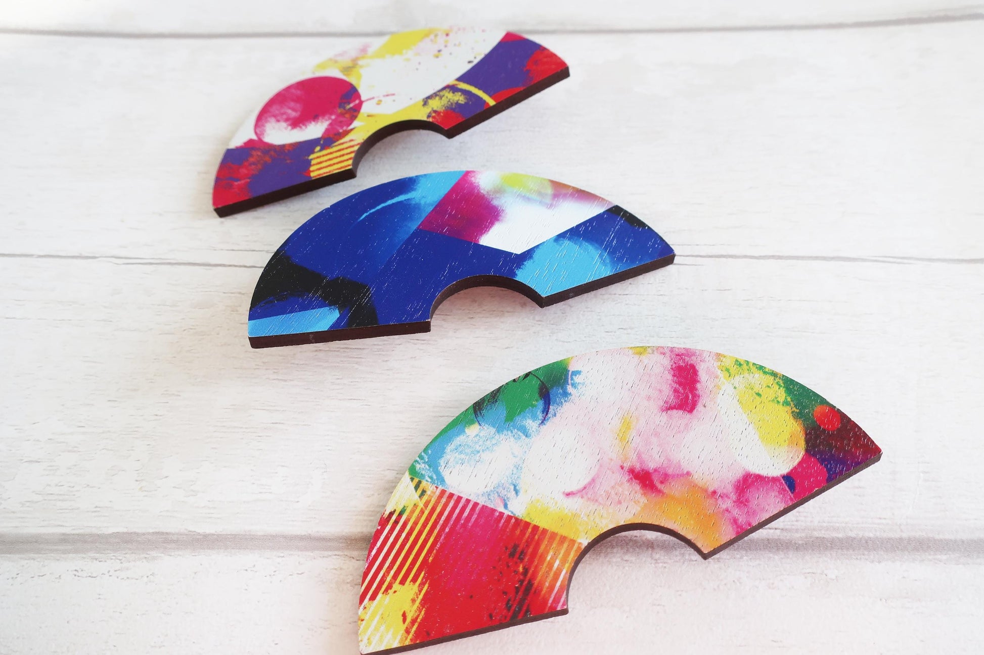 Three colorful, abstract-patterned hairclips on a light wooden surface