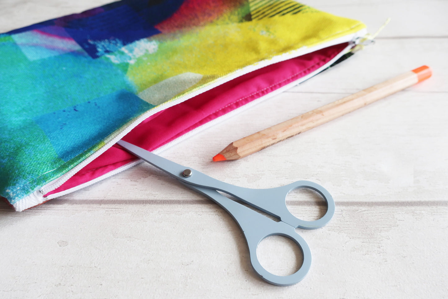 Colorful fabric pouch, scissors, and a pencil on a light wooden surface