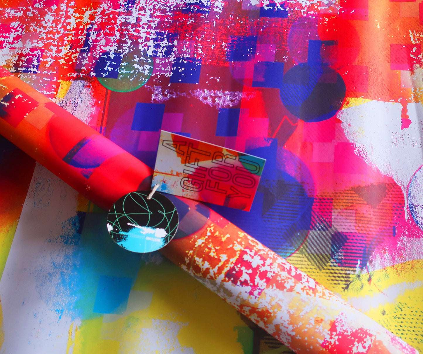 Colorful abstract wrapping paper with a roll of paper and a small card on a textured surface.