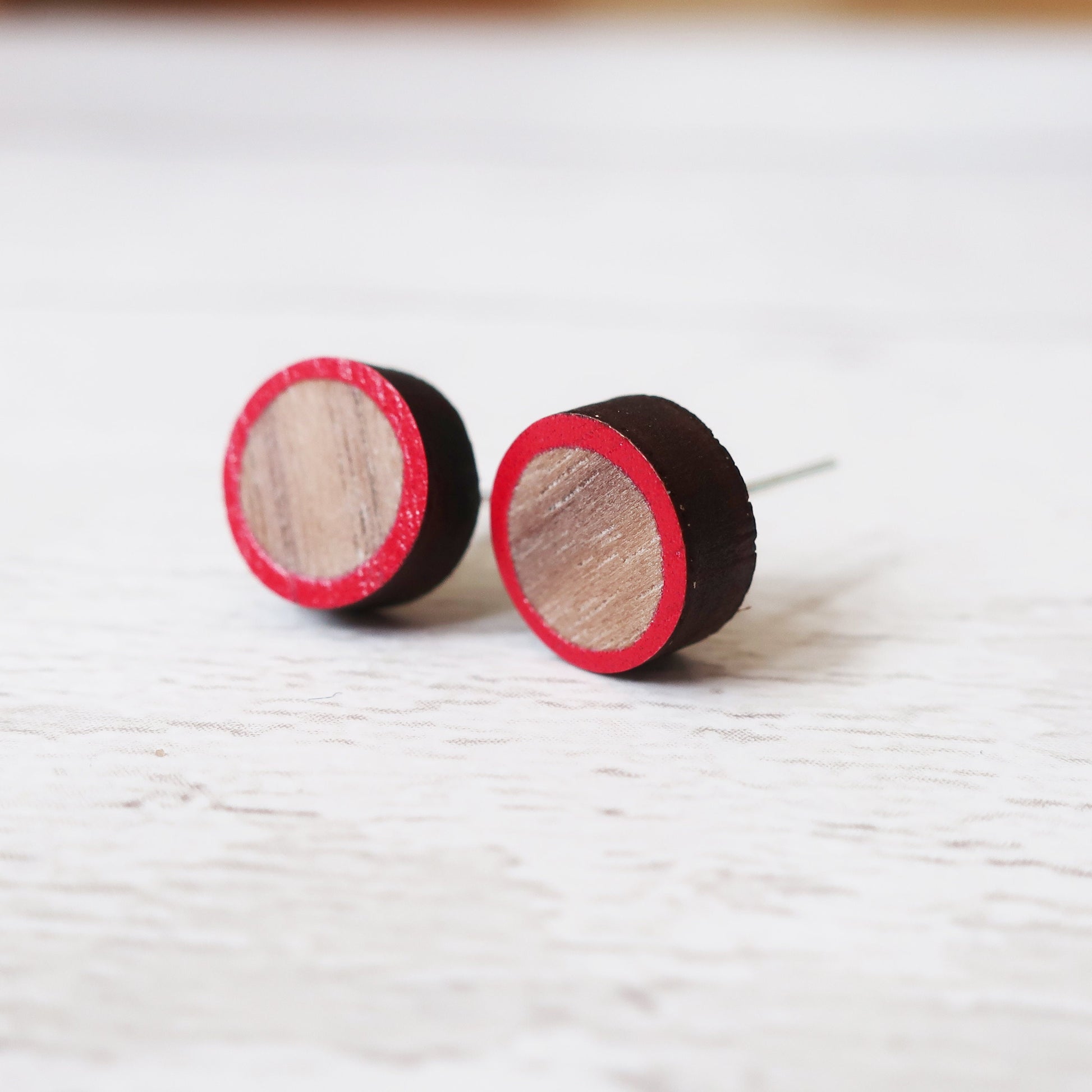 Round wooden earrings with red rim on a white surface