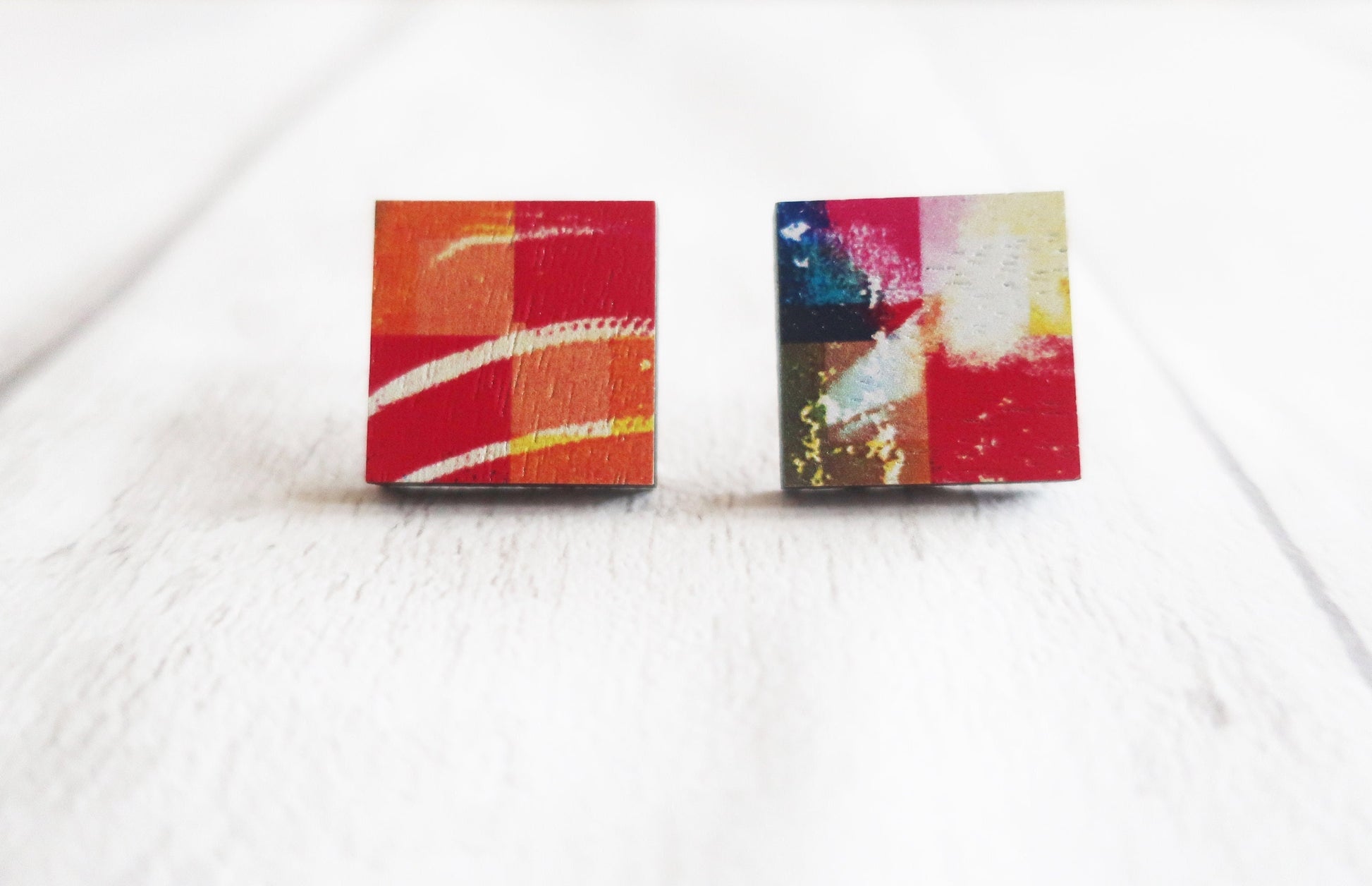 Two square earrings with colorful abstract designs on a white background