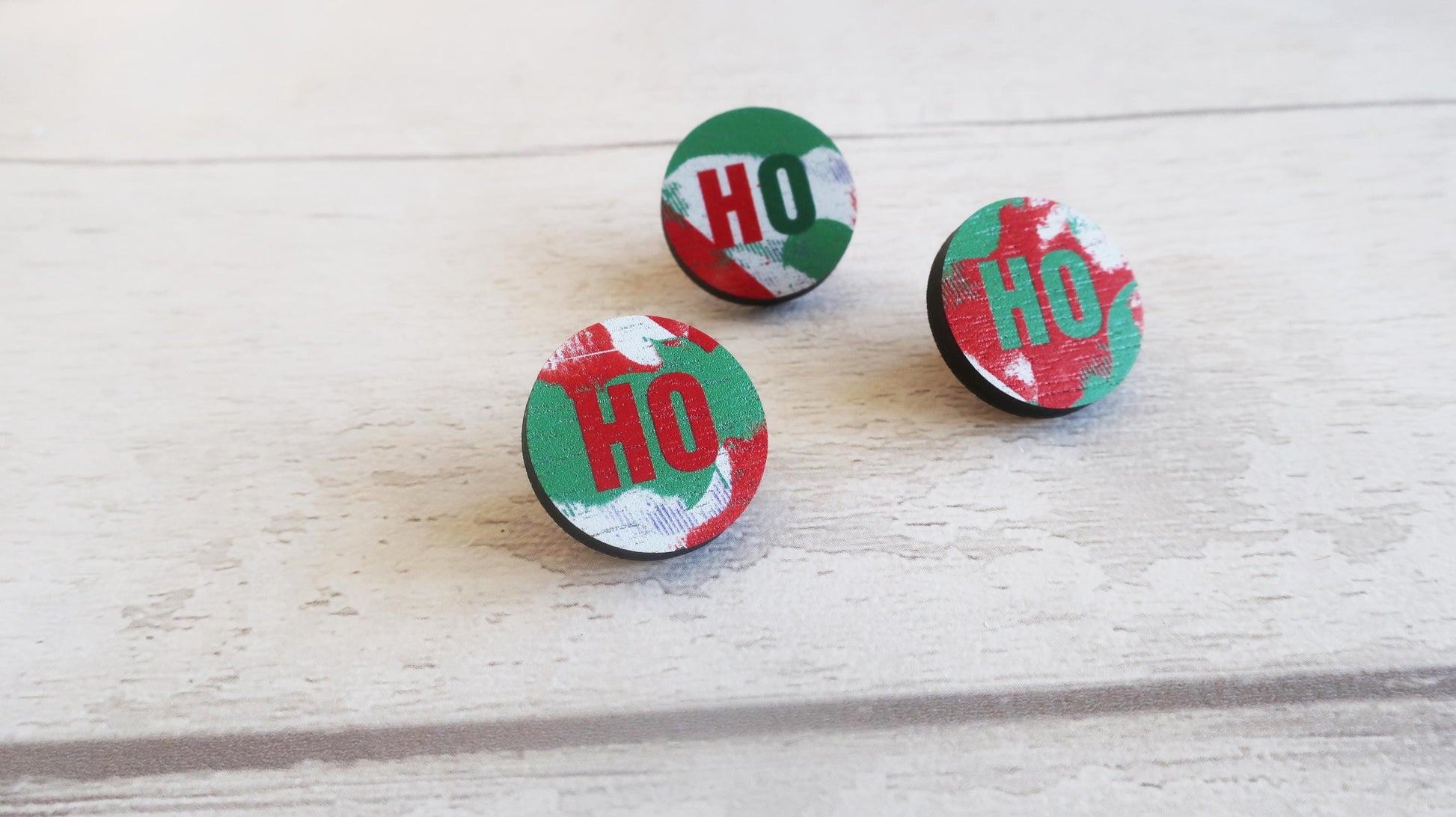 Three circular red and green pin badges with 'HO' text on a light wooden surface.