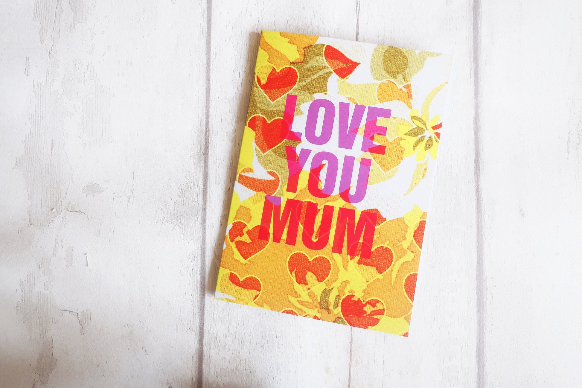 Colorful card with 'Love You Mum' text on a white wooden surface