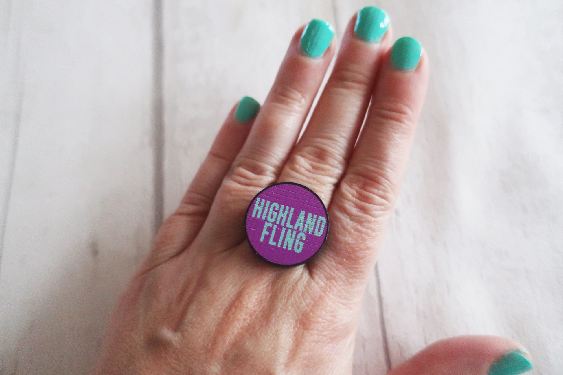 Hand wearing a ring with 'Highland Fling' on a white background