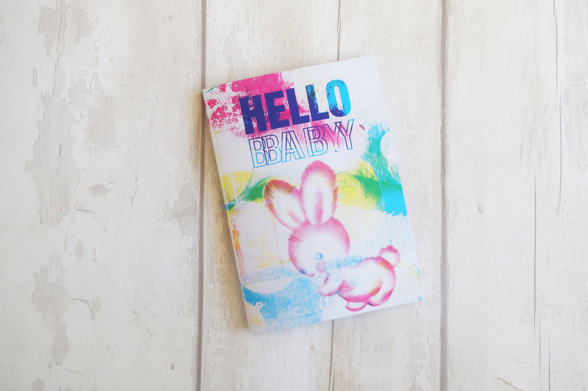 Colorful baby shower card with bunny design and 'Hello Baby' text on a wooden surface