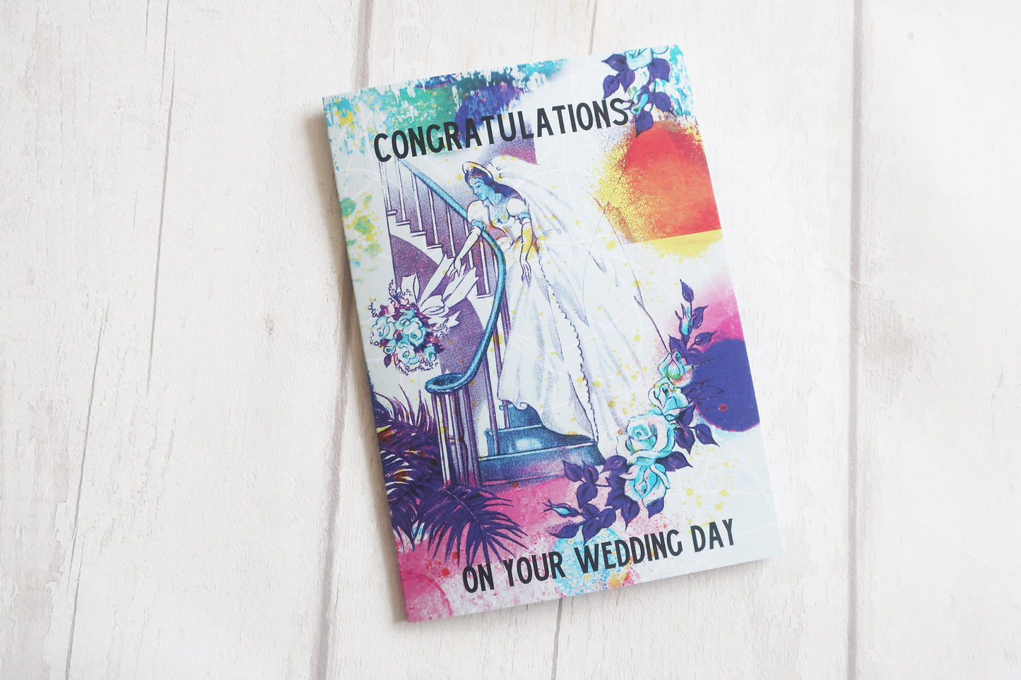 Wedding card with colorful design and 'Congratulations on your wedding day' text on a white wooden surface.