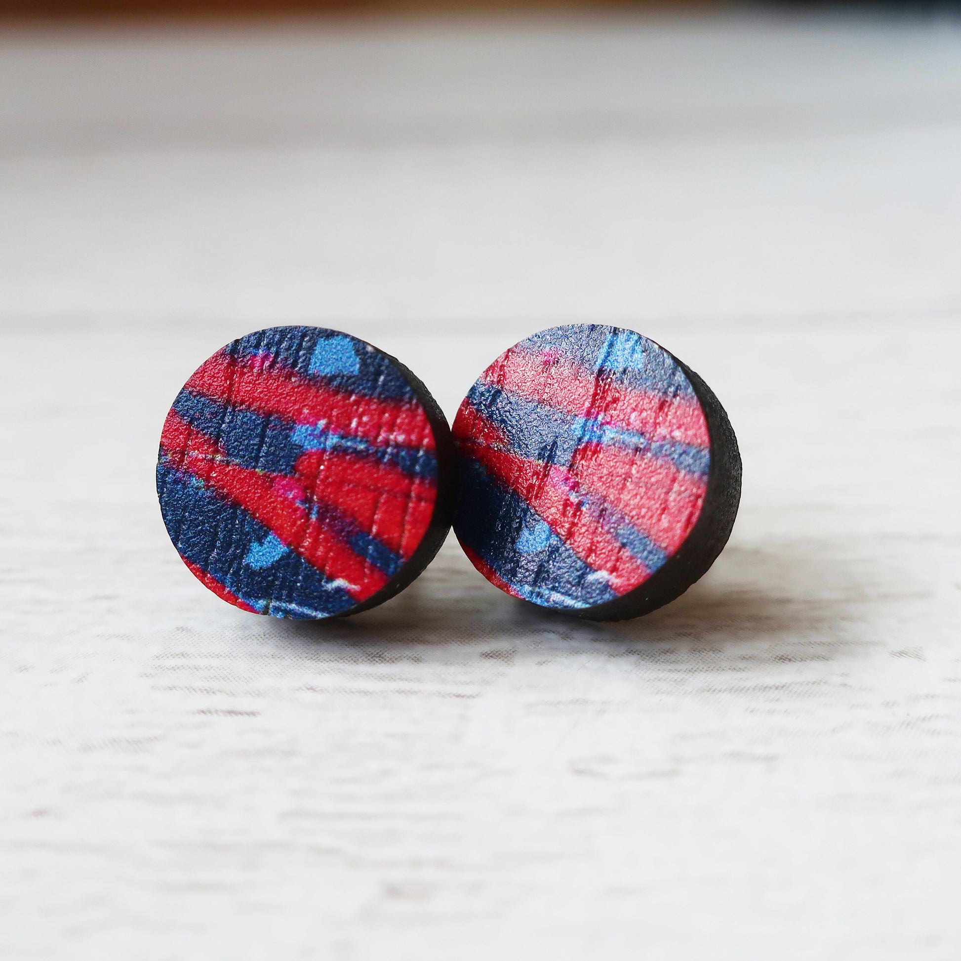 Round earrings with a red and blue plaid pattern on a light wooden surface.