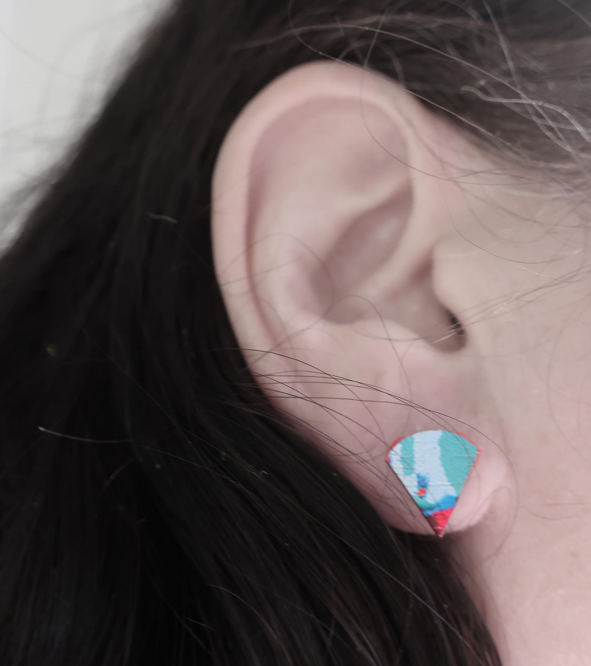 Close-up of an ear wearing a colorful geometric earring with dark hair.