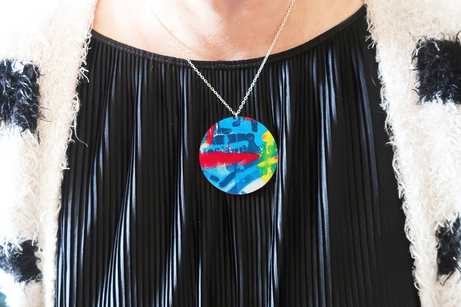 Person wearing a colorful pendant necklace with a black pleated top.