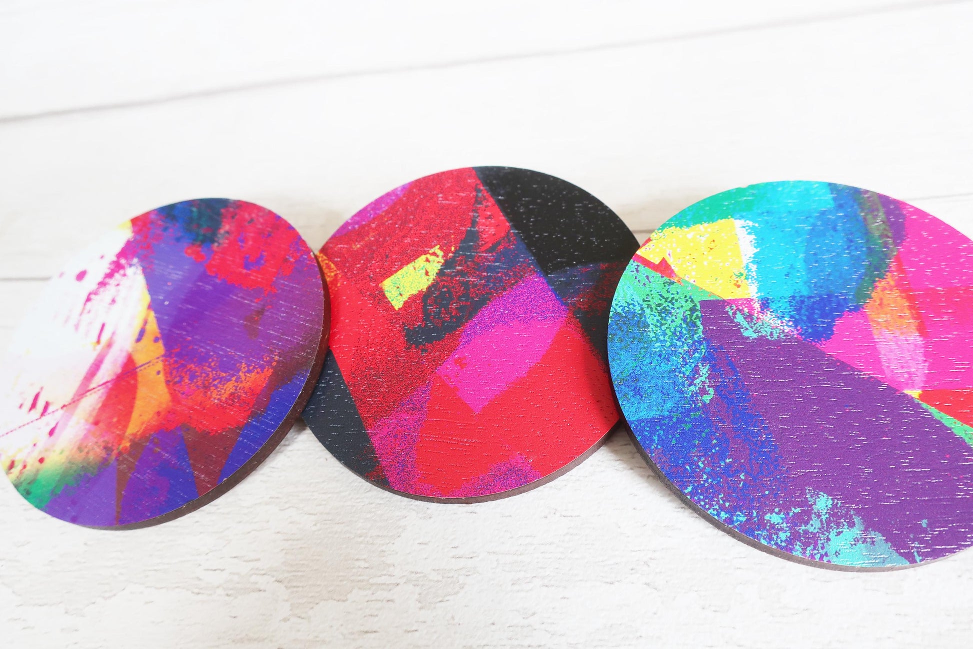 Three colorful circular brooches with abstract designs on a white surface
