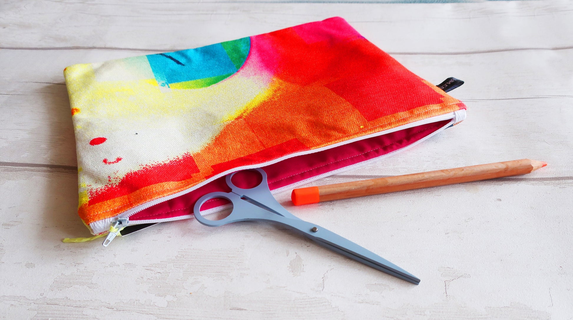 Colorful pencil case with a pen and scissors on a wooden surface
