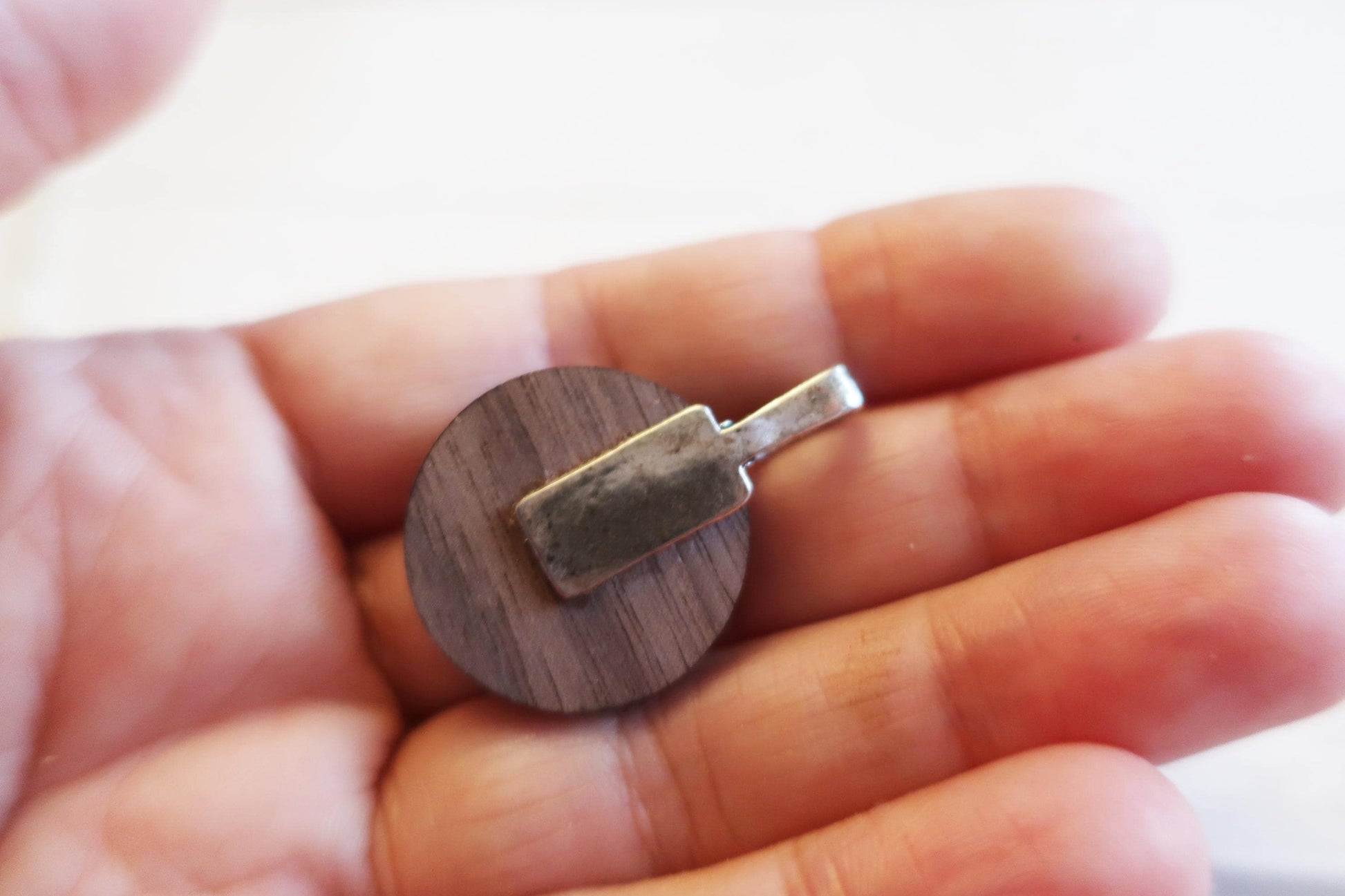 Wooden pendant with metal tag held in a hand against a blurred background