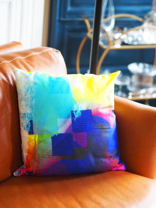 Colorful abstract-patterned pillow on a brown leather couch with a blurred background
