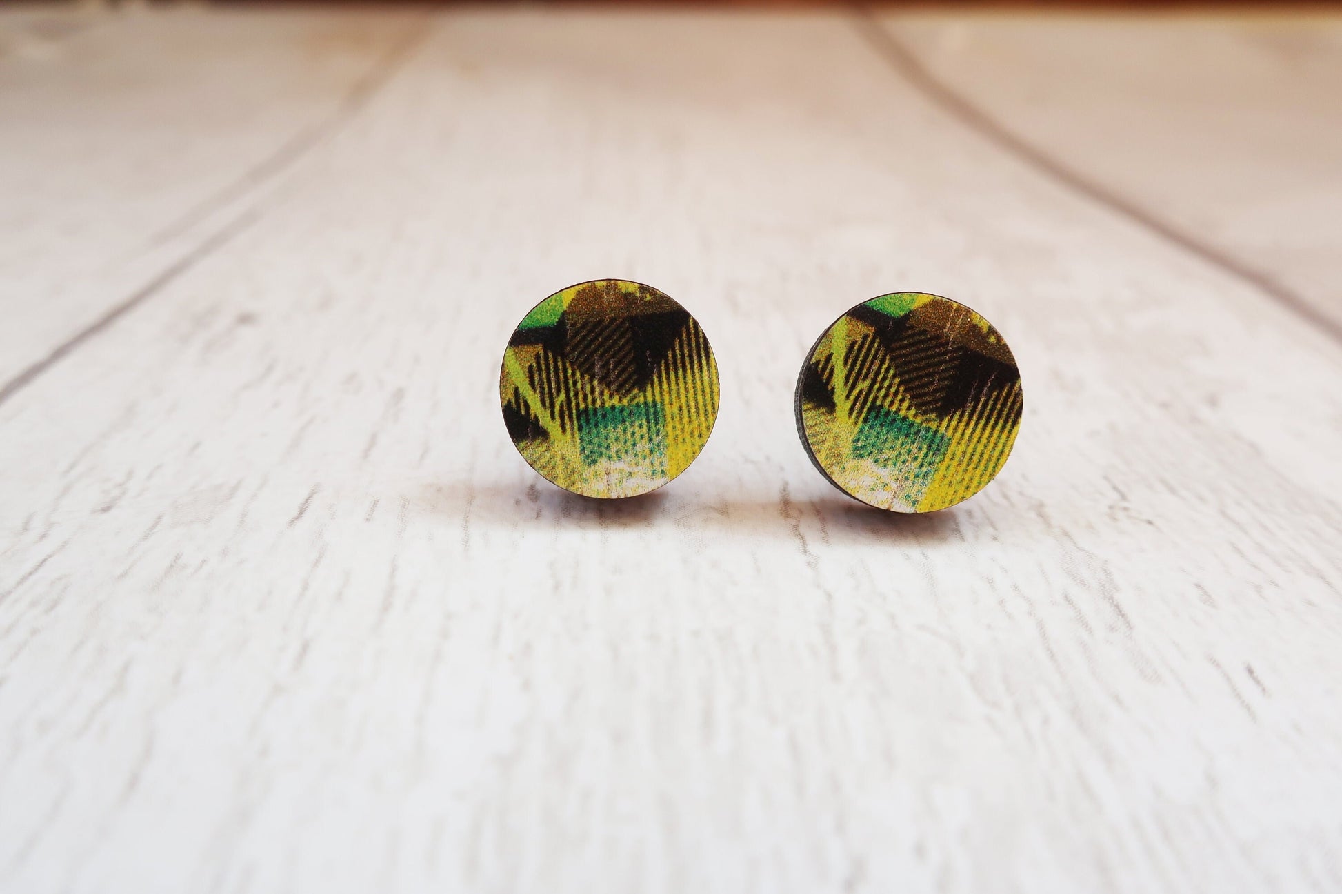 Round earrings with a green and black pattern on a light wooden surface