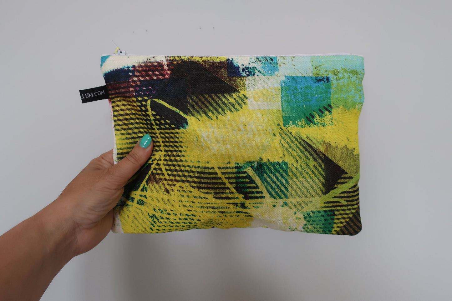 Hand holding a colorful pouch with geometric pattern against a plain background