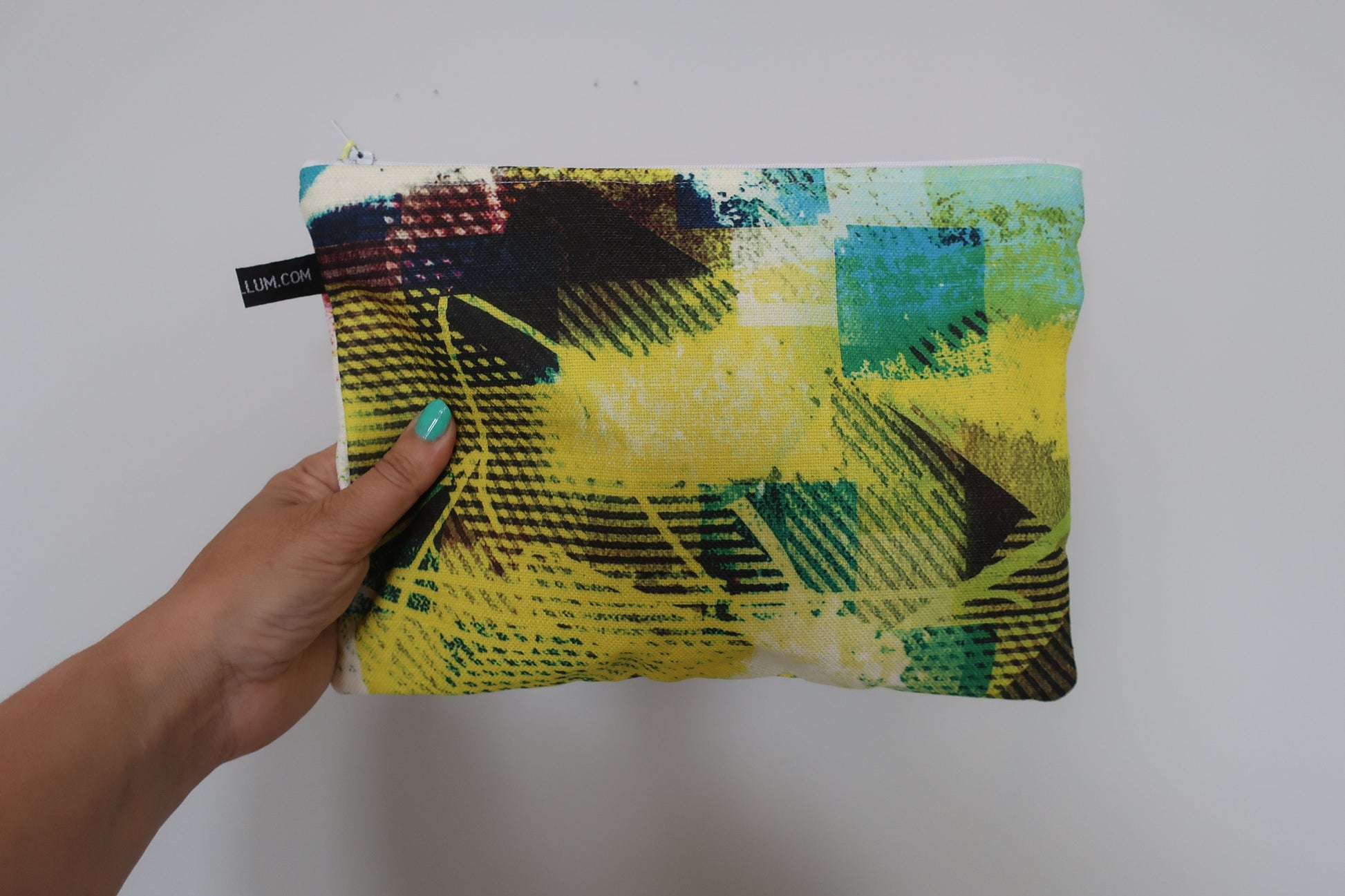Hand holding a colorful pouch with geometric pattern against a plain background