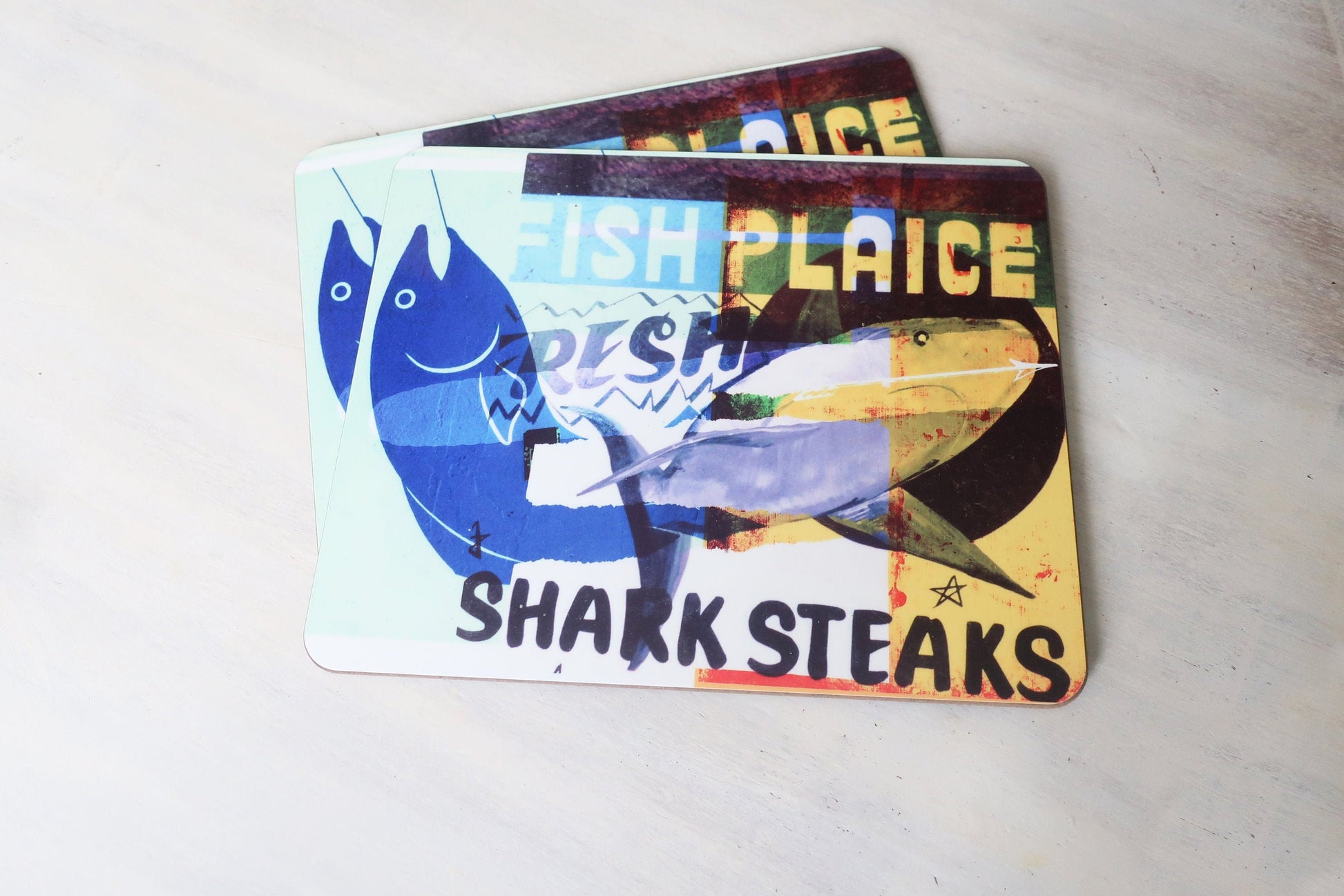 Two fish-themed placemats with colorful designs on a light gray surface.