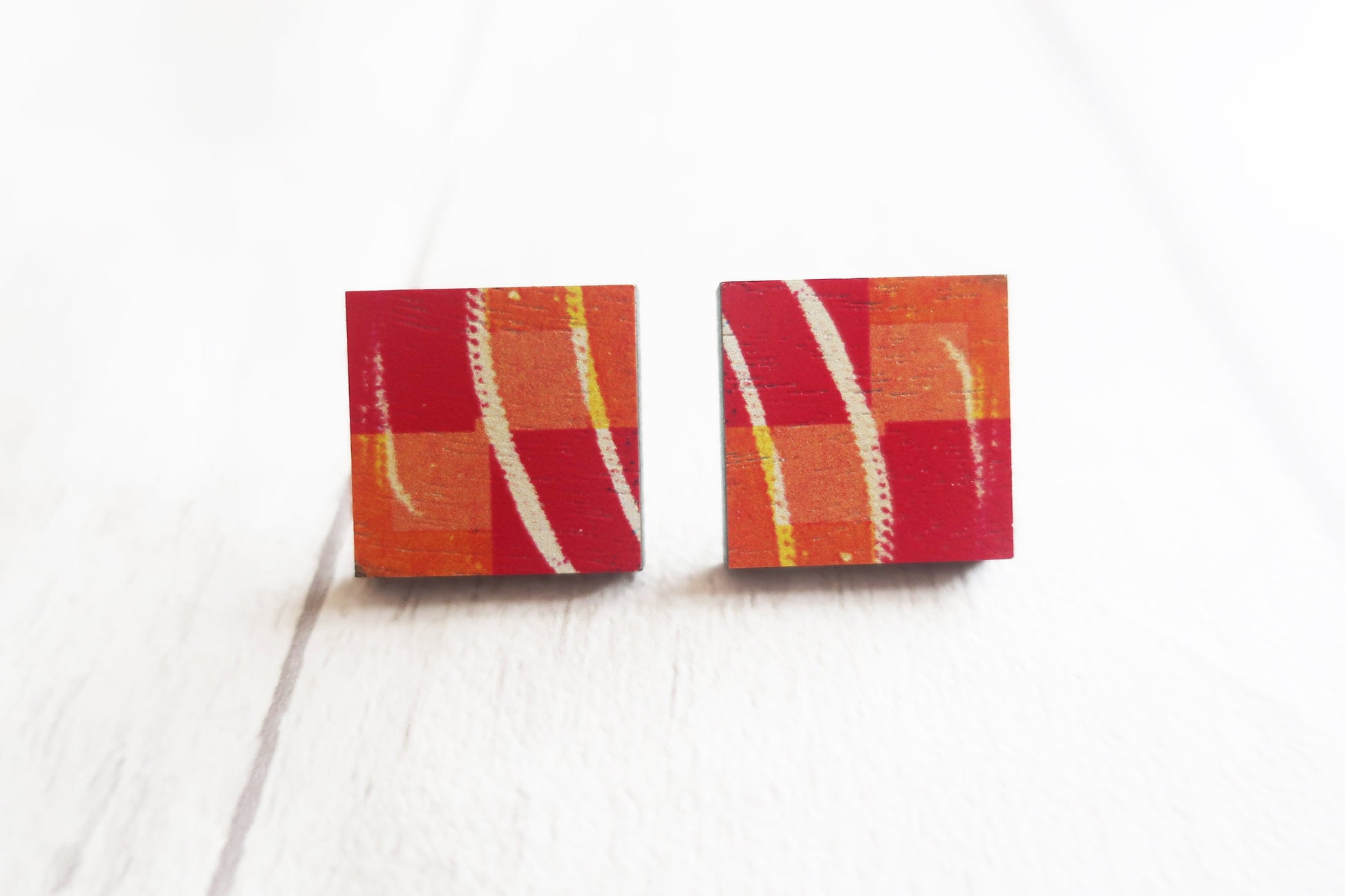 Pair of square earrings with red, orange, and white pattern on a white background