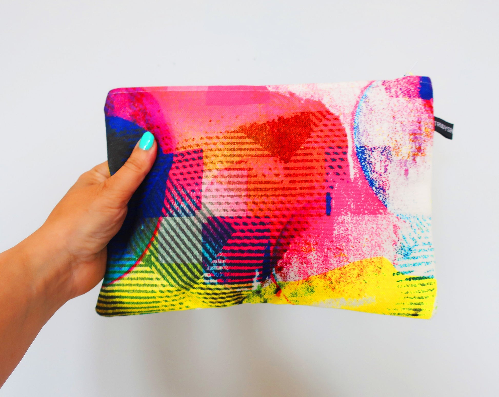 Colorful abstract-patterned pouch held by a hand against a white background