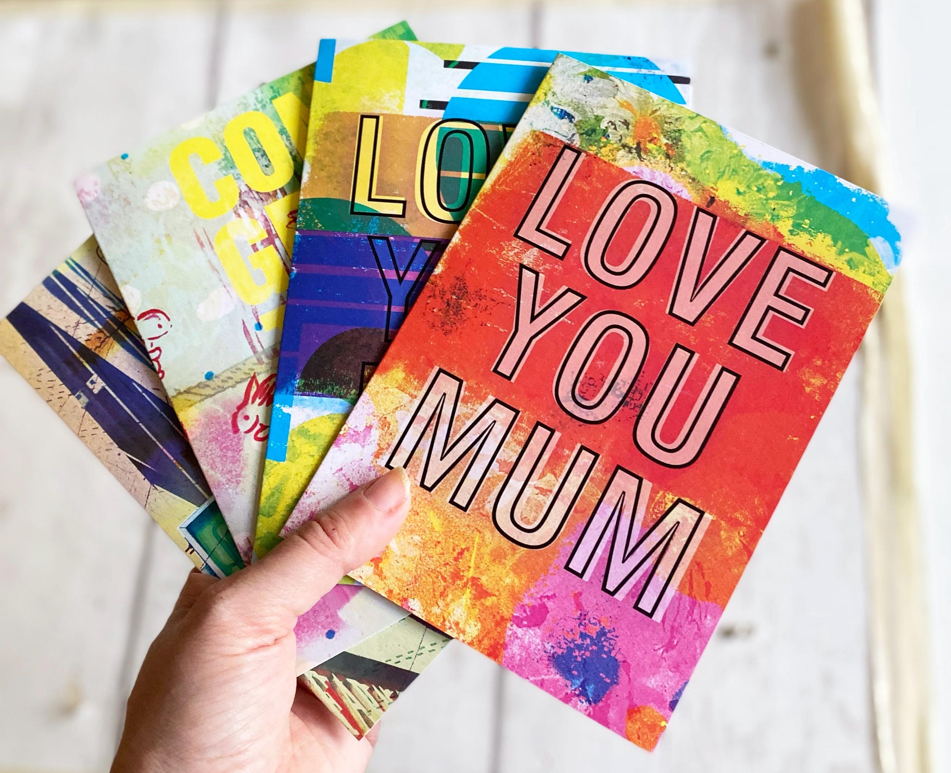 Colorful greeting cards with various messages, including 'LOVE YOU MUM', held by a hand.