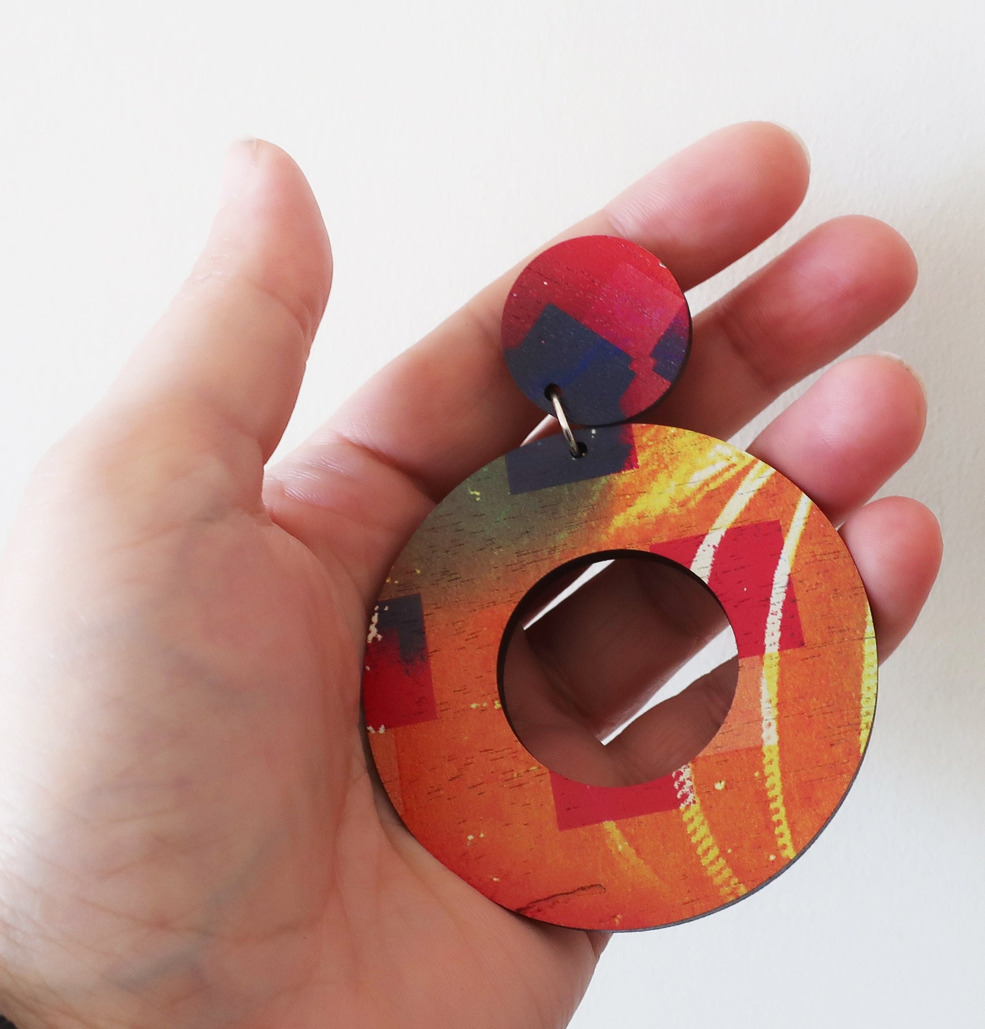 Colorful round earrings held in a hand against a white background