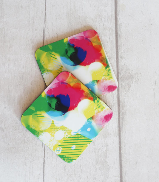 Two colorful abstract design coasters on a light wooden surface