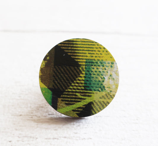 Round green and black patterned pin badge on a white background