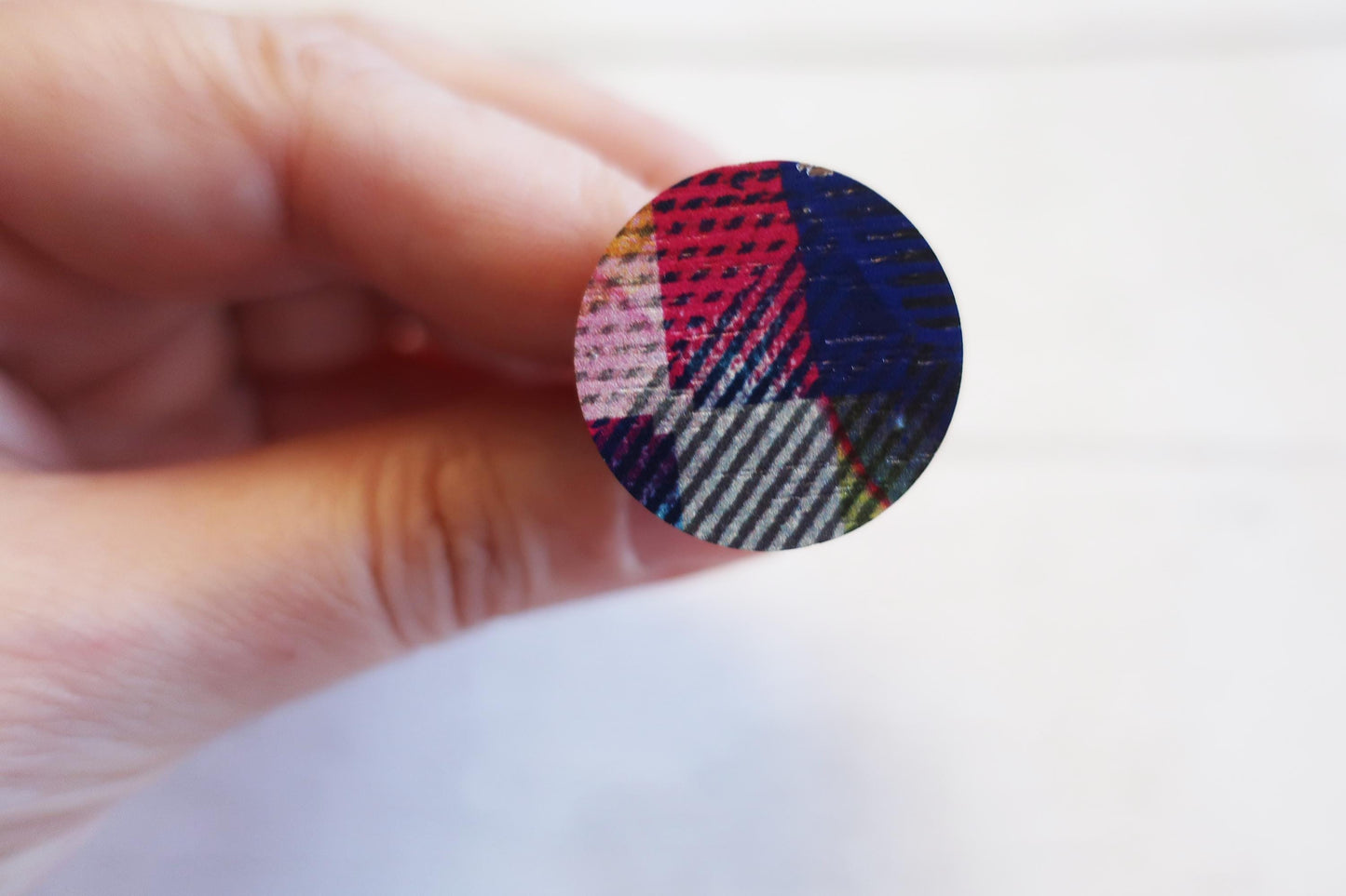 Hand holding a small round ring with plaid pattern on a white background