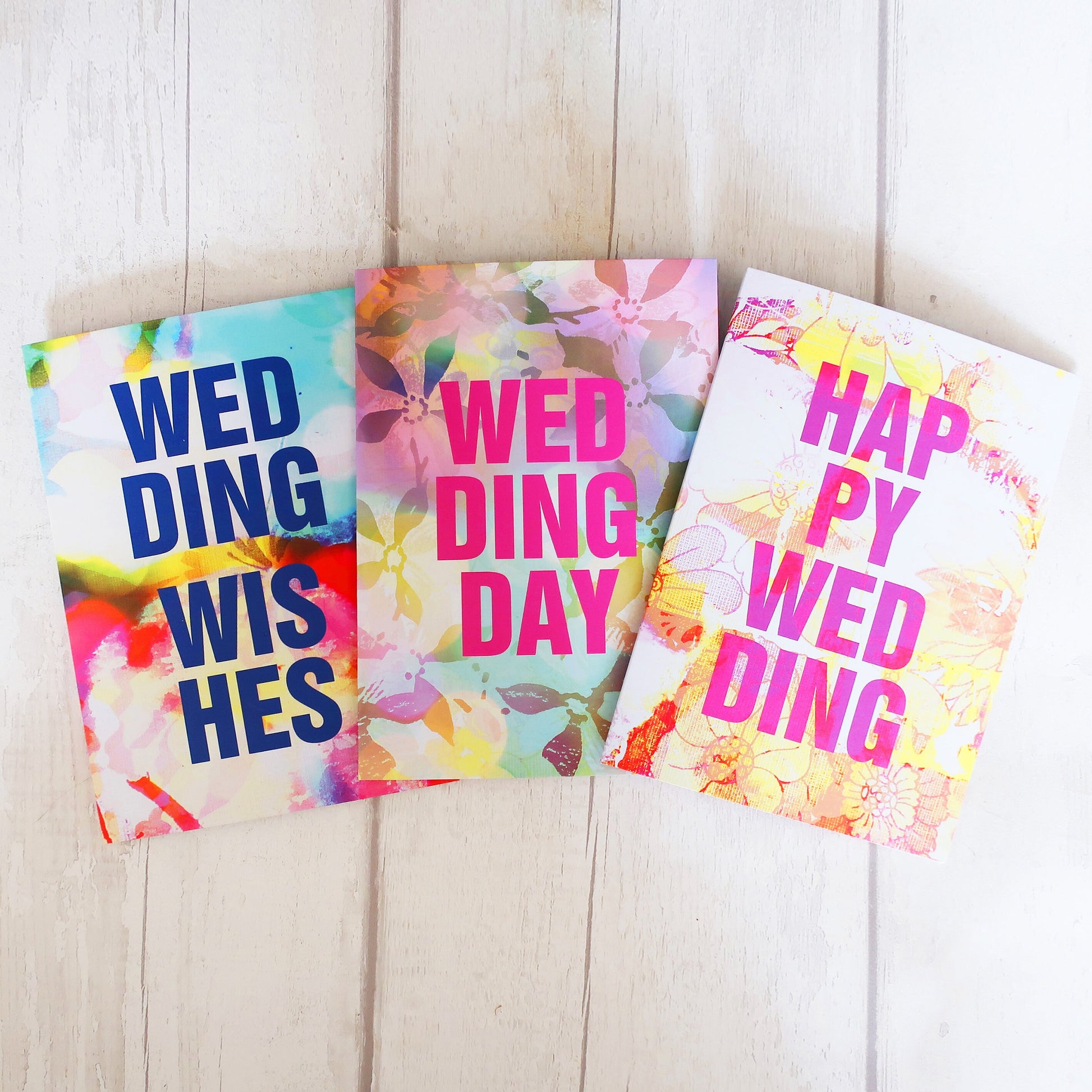 Three colorful greeting cards with wedding wishes text on a wooden surface