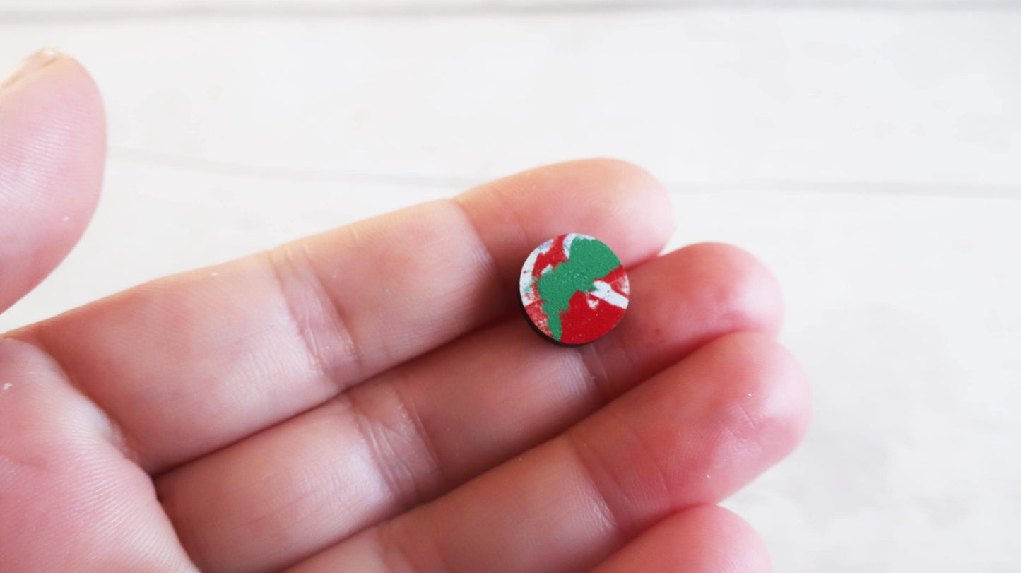 Small round earring with a red and green design held between fingers on a white background