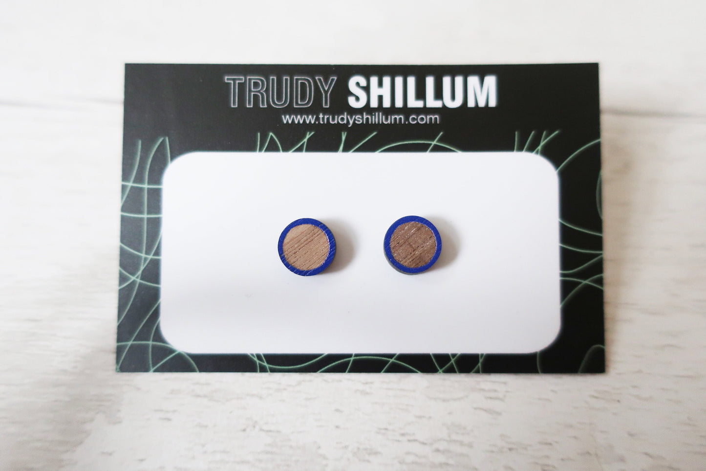 Wooden earrings with blue accents on a Trudy Shillum branded card.