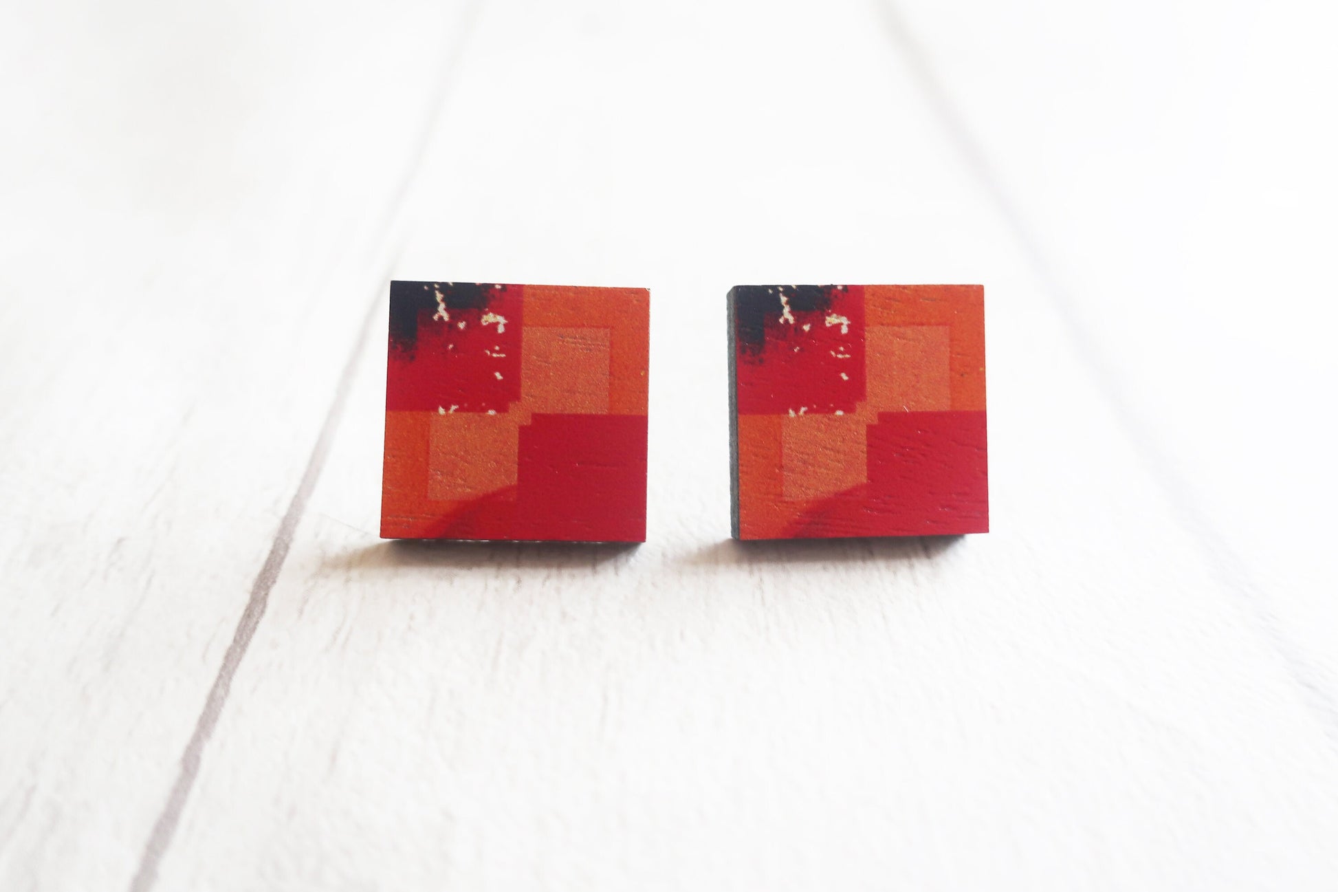 Pair of square earrings with red and black pattern on a white background